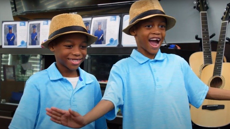 Two Derrico children smiling in matching blue shirts and straw hats