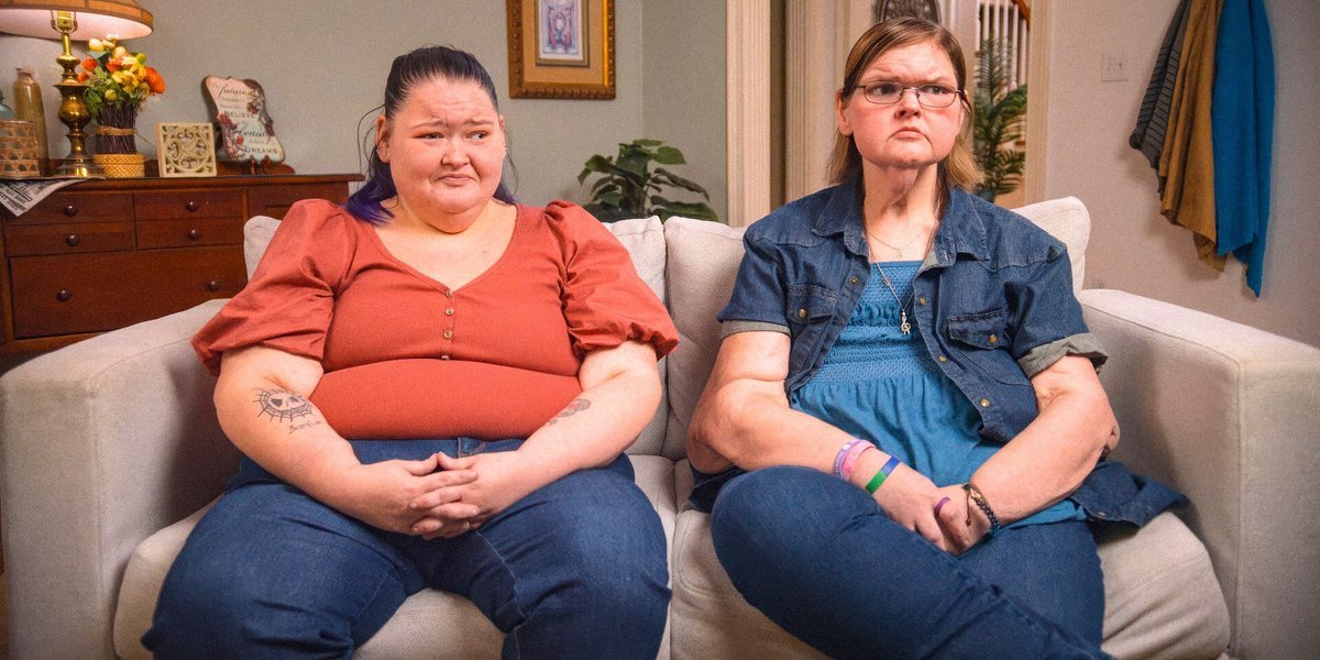 Amy Slaton and Tammy Slaton sitting on a couch, Tammy looking unimpressed, in 1000-LB Sisters