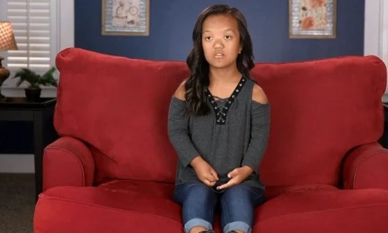 Emma Johnston sitting on a red couch in an earlier season