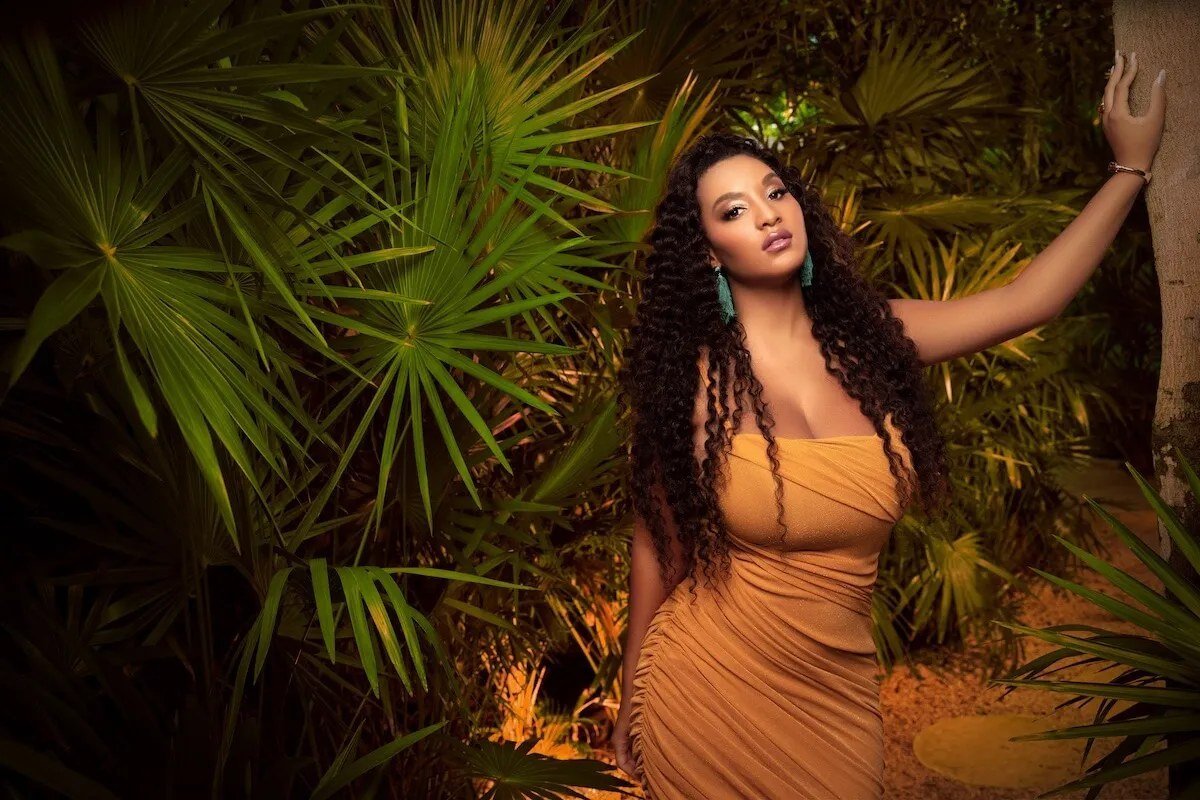 Chantel Everett in a gold dress posing in front of tropical plants