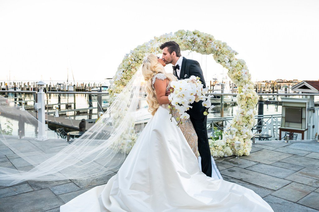 Stacey Silva and Florian Sukaj kissing under a floral wedding arch