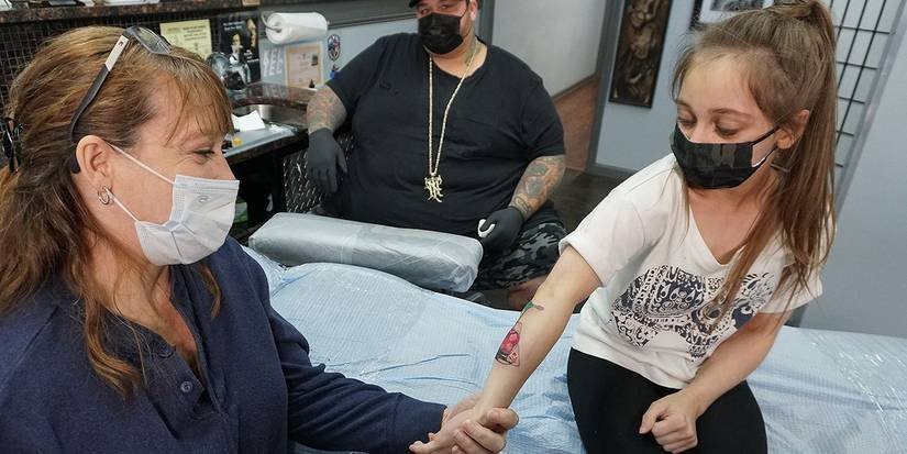 Shauna Rae getting a tattoo in a tattoo parlor while her mother holds her hand