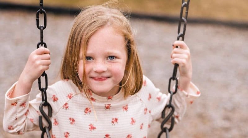 Parker Kate Busby smiling on a playground swing