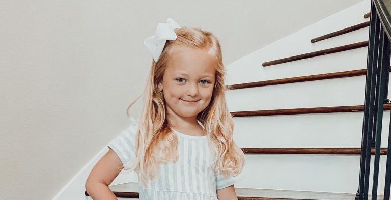 Olivia Busby smiling on a staircase with a big white bow