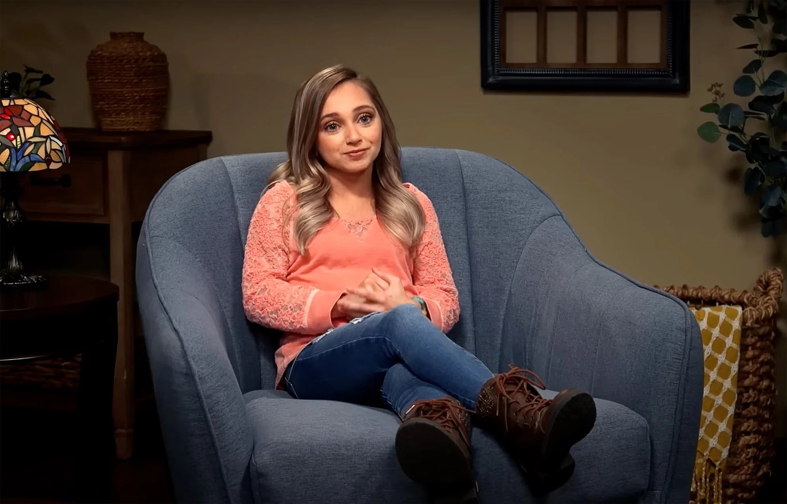 Shauna Rae sitting in a blue armchair in a coral lace top