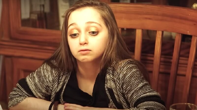Shauna Rae sitting at a dinner table in a black top and patterned cardigan