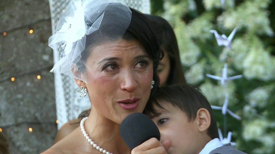 A bride speaking into a microphone at a wedding, with a child beside her