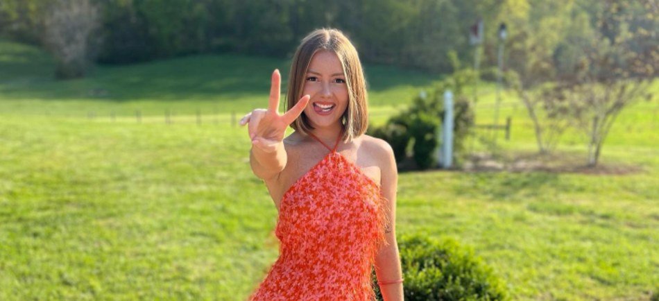 Kara Leona smiling outdoors in a red floral dress