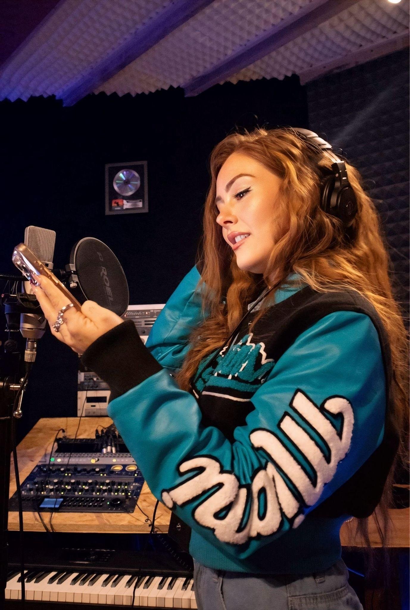 Kara Leona in a recording studio wearing a teal jacket and headphones